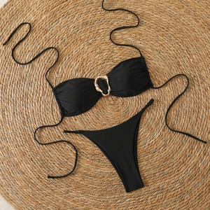 Flat lay of black bandeau bikini set with gold metal ring detail on a straw mat