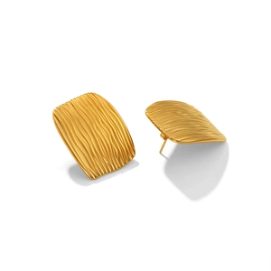 Détail de boucles d'oreilles dorées rectangulaires avec texture ondulée et finition polie