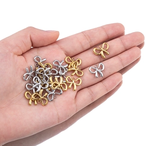 Detailed view of small gold and silver bow charms for DIY jewelry making held in hand