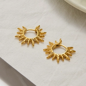 Vue détaillée des boucles d'oreilles soleil dorées texturées sur un tissu en lin blanc