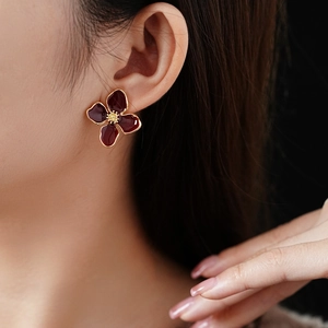 Close-up of vintage flower stud earring in deep red and gold worn by a model