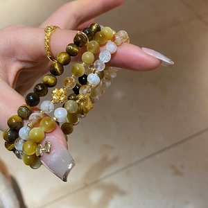 Détail du bracelet en perles d'oeil de tigre avec breloques dorées sur la main