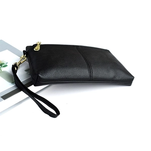 Close-up of black lychee grain leather crossbody bag with golden metal zipper and wrist strap