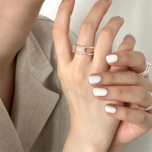 Close-up of minimalist silver chain ring worn on finger with neutral fabric background