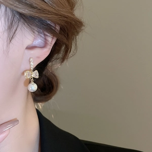 Détail de boucles d'oreilles nœud doré avec oxydes de zirconium et perle blanche sur modèle