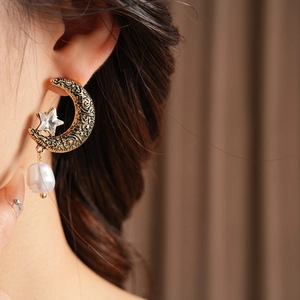 Detail of vintage gold earrings with celestial moon and star design and white pearl pendant
