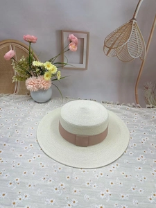 Detail of a beige flat top straw hat with pink ribbon on a floral decorative table