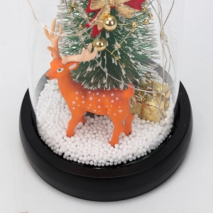 Close-up of Christmas glass dome with miniature pine tree, orange reindeer and snow