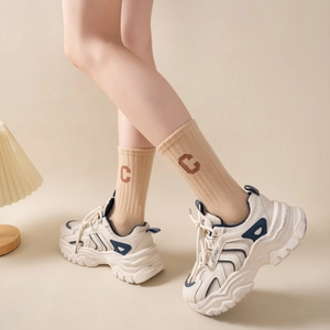 Detail view of cream dad sneakers and embroidered letter socks in a warm lifestyle setting