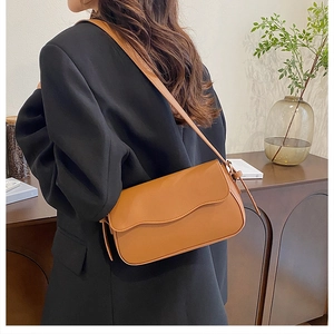 Brown leather shoulder bag with wavy flap design shown on a model in a minimal setting