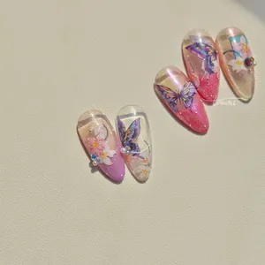 Detail of almond-shaped press-on nails with purple butterfly and pearl decorations