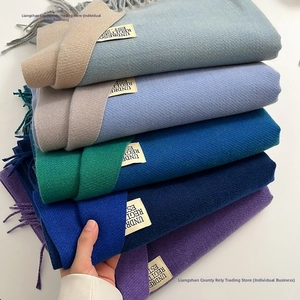 Close-up of double-sided cashmere-like scarves with tassel edges and brand labels