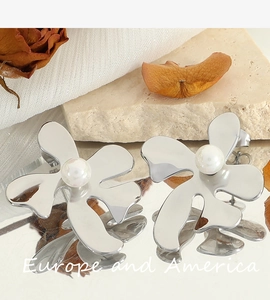 Détail de boucles d'oreilles fleur argentée avec perle sur un socle miroir