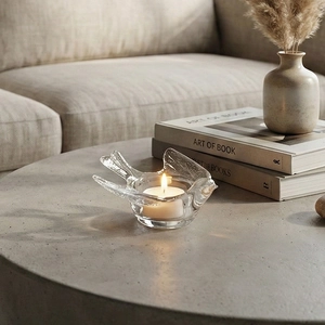 Transparent bird-shaped glass candle holder with tealight on a modern stone tabletop