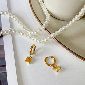 Detail showing gold hoop earrings with yellow square zircon pendant and pearl necklace
