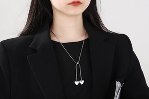 Silver snake chain necklace with dual heart pendants worn by a model in a black suit