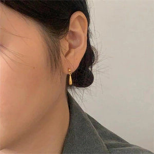 Dettaglio degli orecchini a goccia in oro lucido indossati con un design minimalista chic