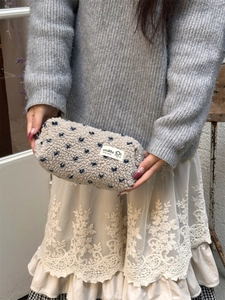 Gros plan d'une trousse en peluche blanc cassé avec motifs de cœurs bleus et étiquette tissée