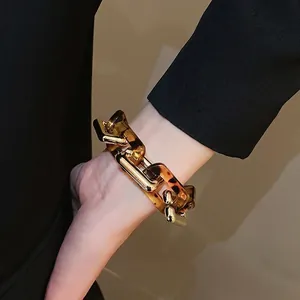 Bracciale a catena in resina leopardata e oro indossato da una modella in blazer