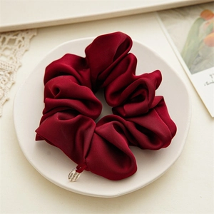 Detail of premium burgundy satin scrunchie with silver logo tag on a ceramic plate