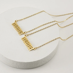 Gold stainless steel MAMA letter necklaces layered on a white circular display base