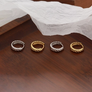 Macro shot of silver and gold hoop earrings with wheat leaf patterns on wooden tray