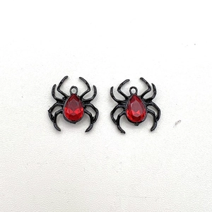 Detail of two vintage black spider charms with red teardrop rhinestones on white background