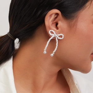 Detailed close-up of bow-shaped faux pearl tassel earrings worn on a model