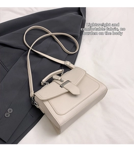 Close-up of beige lychee grain leather handbag with metallic buckle and shoulder strap