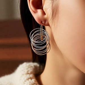 Detail of gold and silver multi-layer hoop earrings with diamond-cut texture on model