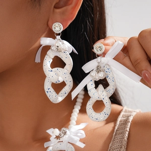 Detail of white acrylic bow earrings with blue ink spots and pearl drops on model