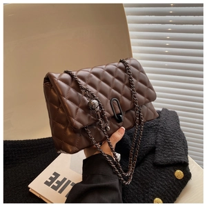 Detail of a brown quilted leather chain bag featuring dark metal hardware and decorative ball