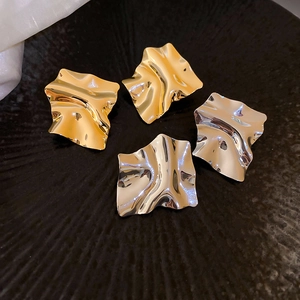 Close-up of irregular wavy gold and silver stud earrings on a black textured surface