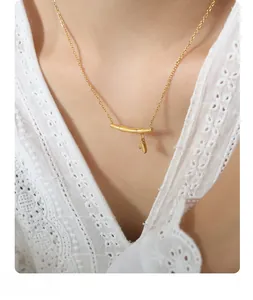 Détail d'un collier doré avec pendentif en bambou et petite breloque de feuille