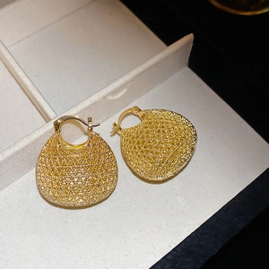 Macro shot of gold hollow oval earrings with woven mesh texture on white silk