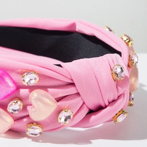 Primer plano detallado de diadema de satén rosa con nudo, pedrería y corazones