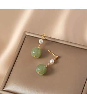 Detailed close-up of retro freshwater pearl and green jade earrings on silk fabric