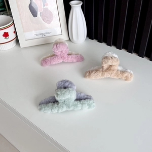 Three plush two-tone claw clips in pink, camel, and mint green on a white table