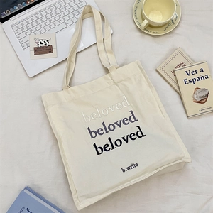 Detail of cream canvas tote bag with beloved embroidery, styled with laptop and coffee cup