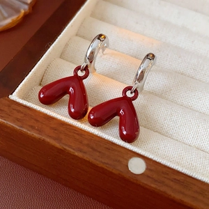 Macro shot of red heart drop earrings with silver clasps on beige velvet jewelry box