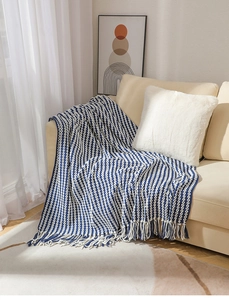 Detail view of blue and white knit blanket with decorative tassels on a beige sofa
