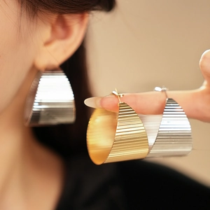 Detailed view of large gold and silver chunky hoop earrings with striped texture surface