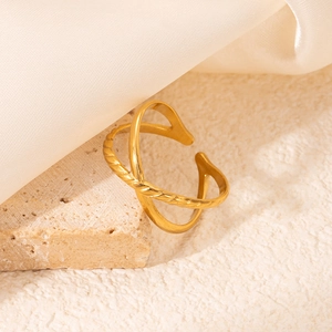 Gros plan d'une bague croisée dorée avec textures tressées et lisses sur tissu en soie