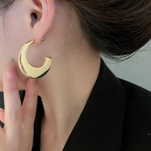 Close-up of a model wearing large thick gold C-shaped hoop earrings with a mirror finish