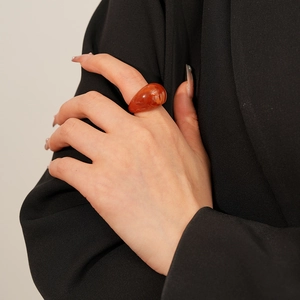 Détail d'une bague goutte en résine ambre sur la main avec fond noir contrasté