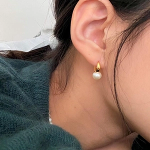 Close-up of a single pearl earring on golden hoop worn by a model in soft lighting