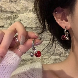 Close-up of red cherry resin earrings with silver needle shown on a model's ear