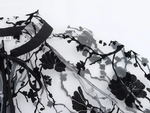Detail of sheer mesh blouse featuring floral flocking patterns and neck tie design