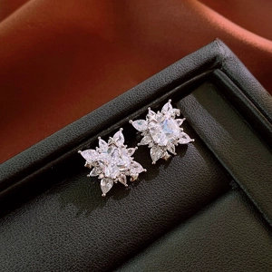 Detailed close-up of square zircon flower ear clips on elegant brown silk and black leather