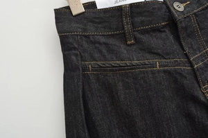 Dettaglio jeans in denim nero con cuciture arancioni a contrasto e bottone metallico